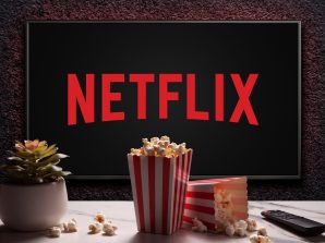 Netflix logo on TV with popcorn boxes, reomote control and home plant on the table. Netflix streaming service for watching videos. Moscow, Russia - November 29, 2022.