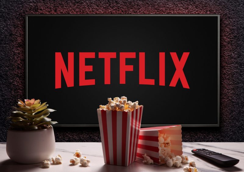 Netflix logo on TV with popcorn boxes, reomote control and home plant on the table. Netflix streaming service for watching videos. Moscow, Russia - November 29, 2022.